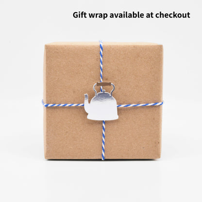 The gift wrap features a paper cutout of a silver teapot. 