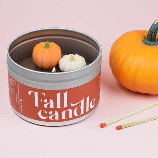 The Fall Candle has a smoky bonfire scent and two miniature wax pumpkins on its surface.